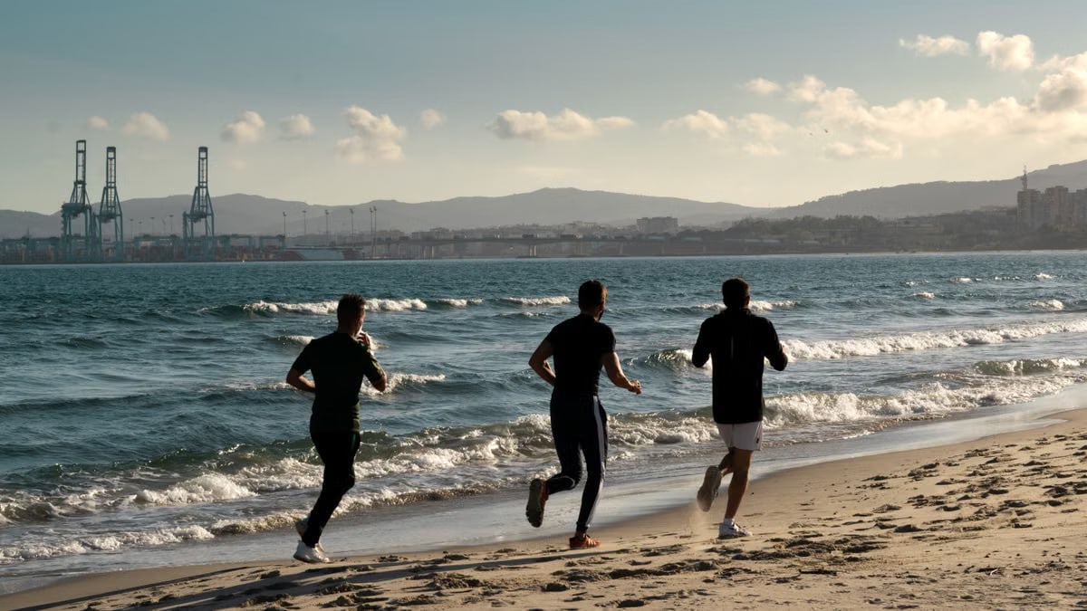 Three men jogging along a scenic beach, embracing a healthy lifestyle under a clear sky.